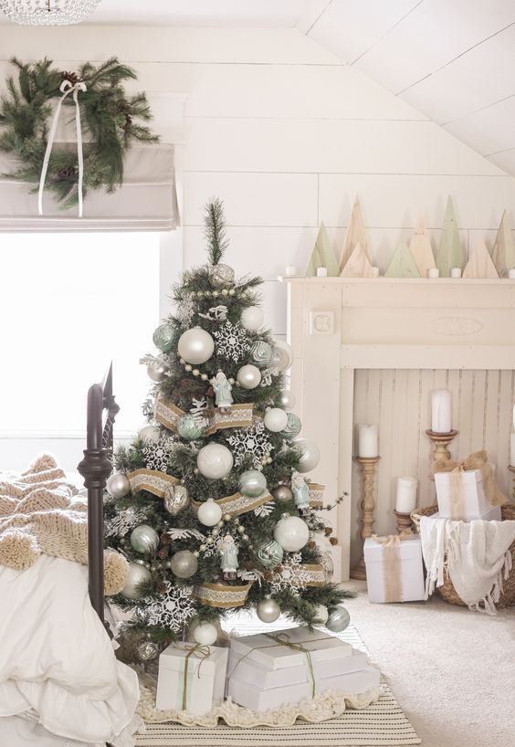 a white vintage Christmas space with a tree decorated with white, silver and green ornaments, a burlap and lace ribbon and white snowflakes, pillar candles and plywood trees