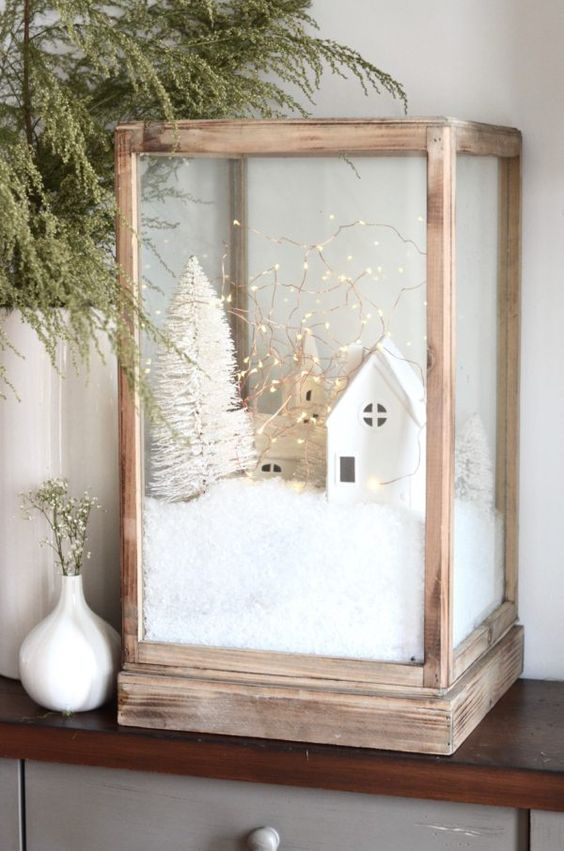 an oversized wooden lantern with a little Christmas scene - faux snow, two white houses and a white bottle brush Christmas tree plus lights