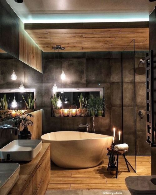 a beautiful moody bathroom clad with wood and with dark tiles, with a chic bathtub, a floating wood slab vanity and candles around