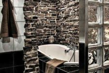 a bold bathroom clad with natural dark stone and with black tiles that are highlighted with white grout