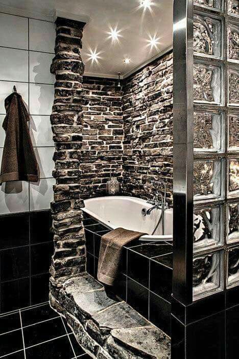 a bold bathroom clad with natural dark stone and with black tiles that are highlighted with white grout