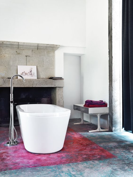 a bold bathroom with catchy floor, a large fireplace of concrete, a metal bench, bright textiles and artwork