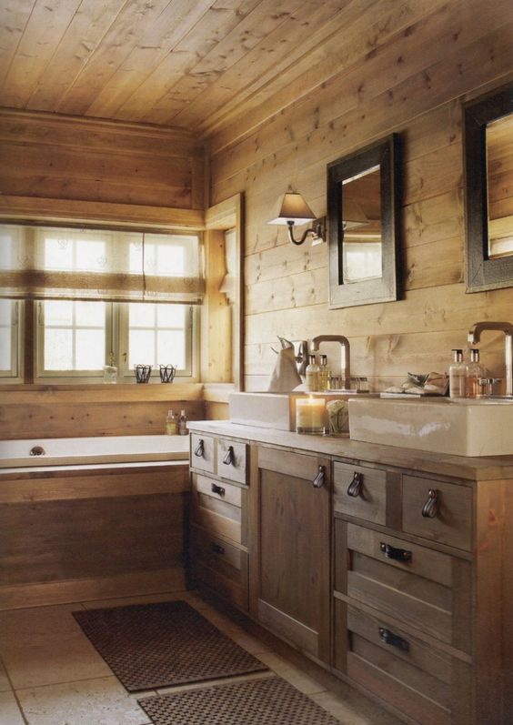 a cabin bathroom clad with wood, with a bathtub clad with wood, a double vanity of wood and two mirrors is welcoming