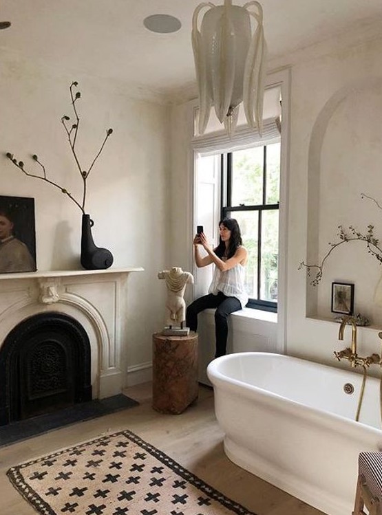 a chic Parisian space in neutrals, with blakc touches, a faux fireplace, a statement chandelier and a sculpture