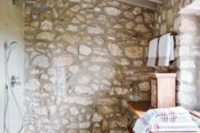 a chic attic bathroom with a rough stone wall, a sleke wooden vanity and enough natural light incoming