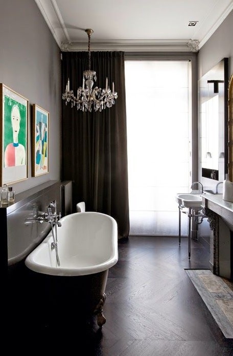 a chic contemporary meets vintage bathroom in chocolate browns, with a crystal chandelier, a clawfoot bathtub and a free-standing sink