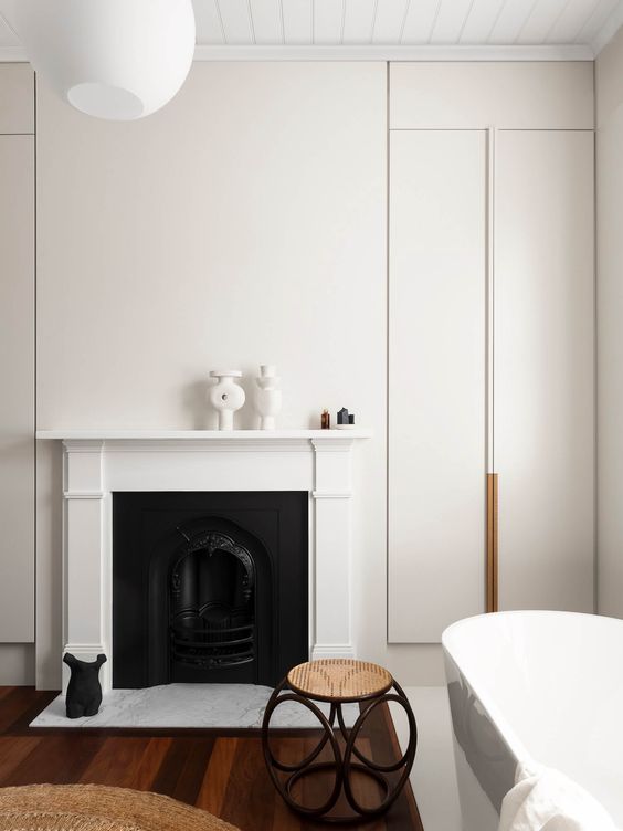 a chic modern neutral bathroom with a fireplace, an oval tub, a cane side table, a pendant lamp and some refined decor