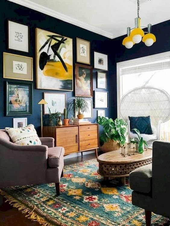 a chic navy living room with touches of yellow, a fringe rug, mismatching furniture and a peacock chair plus a gallery wall