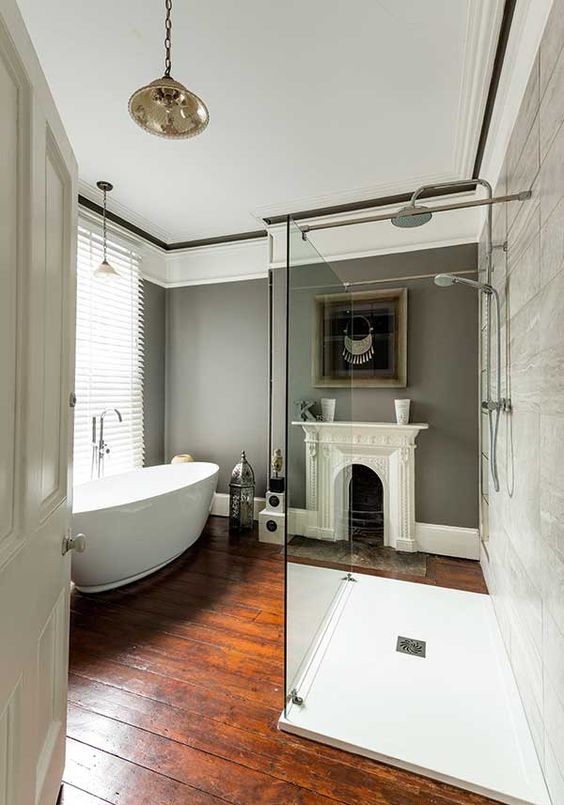 a chic vintage bathroom with grey walls, a shower space, an oval tub, pendant lamps and a non workign fireplace plus art