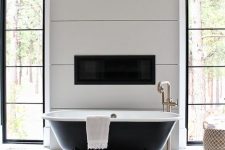 a chic vintage bathroom with white geo tiles, a black clawfoot bathtub, a built-in fireplace and a chic chandelier