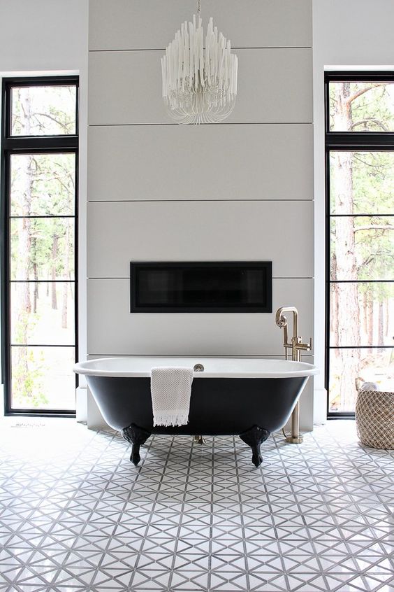 a chic vintage bathroom with white geo tiles, a black clawfoot bathtub, a built in fireplace and a chic chandelier