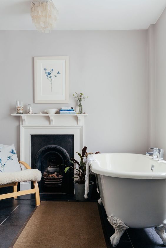 a delicate bathroom with grey walls, a grey clawfoot bathtub, a wooden chair, blue blooms printed on the wall and pillow