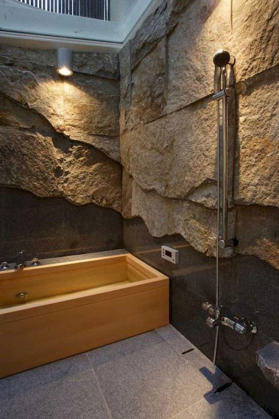 a gorgeous contemporary bathroom done with rough stone walls covered with glass and a wooden bathtub