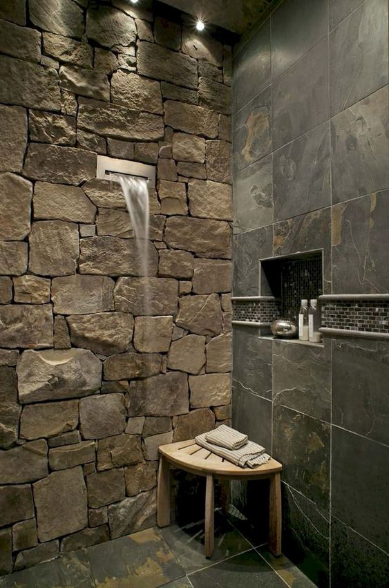 a gorgeous contemporary shower done with a natural stone wall, wall tiles imitating stone and a waterfall shower