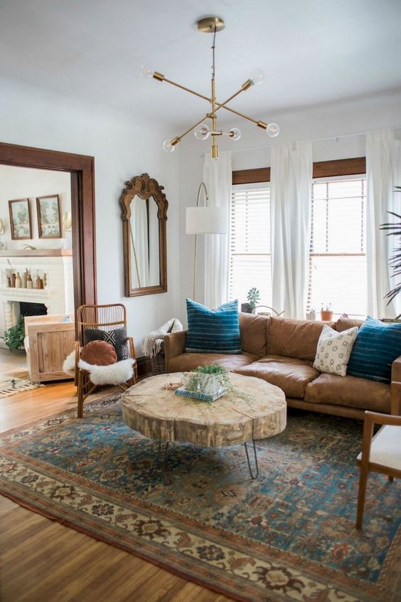 a mid-century modern space with a large leather sofa, a wood slice table, rattan chairs and a creative chandelier