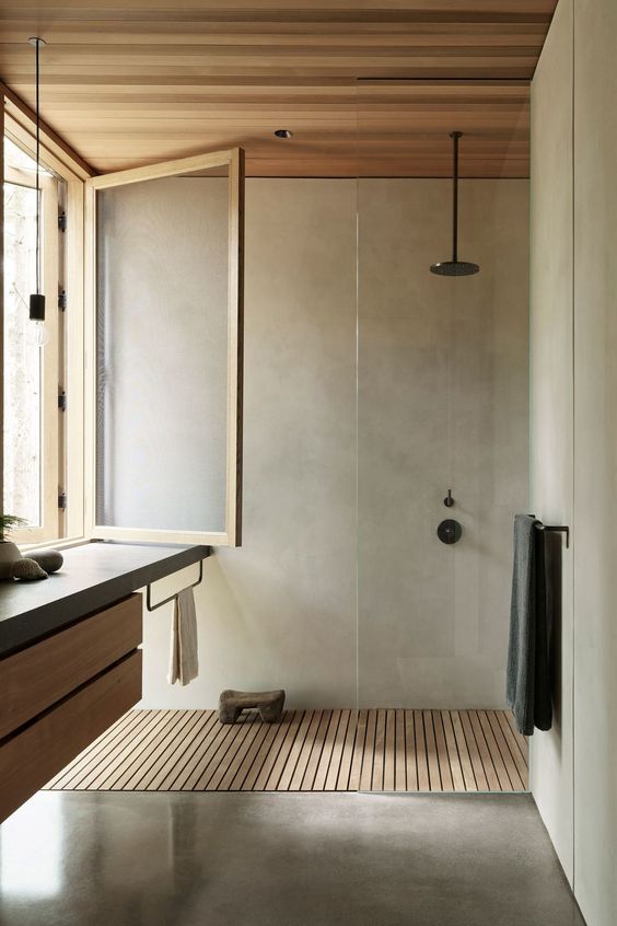 a minimalist bathroom clad with light stained wood and with concrete, with black fixtures and a vanitu with a concrete countertop