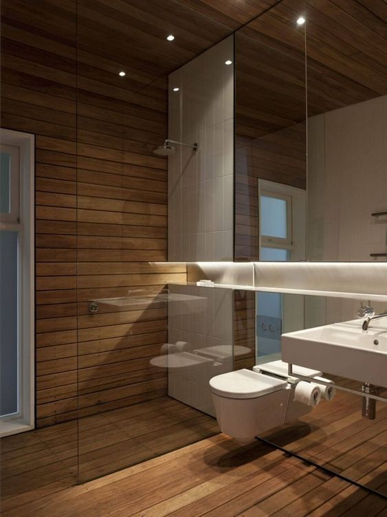 a minimalist bathroom clad with light stained wood, with a mirror wall and white appliances is pure luxury and invites in