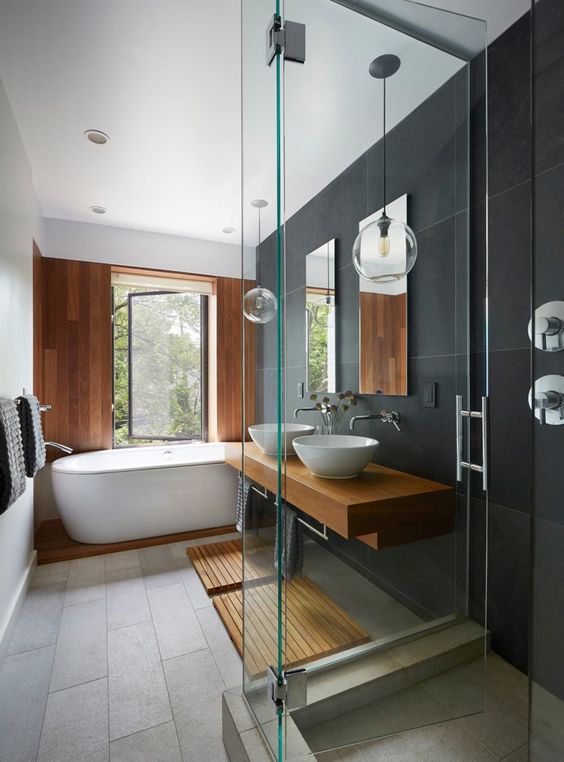 a minimalist bathroom done with grey and black tiles, with a wooden accent wlal and platform, a wooden vanity and mats plus pendant lamps