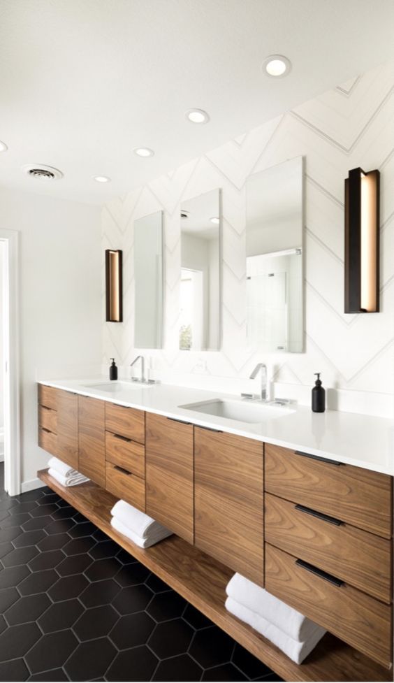 a modern bathroom done with black and white tiles, with a stained wooden vanity and a trio of mirrors, with built-in lights