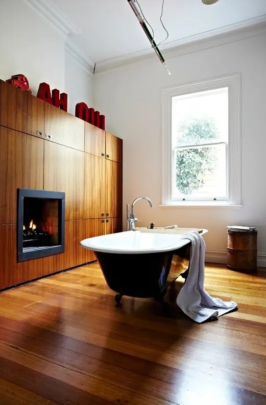 a modern bathroom with a wooden floor, a wooden storage unit that includes a fireplace, monograms and a black vintage bathtub