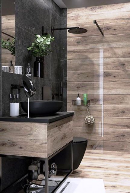 a moody bathroom clad with light stained wood and with black tiles, a chic vanity with a black sink and black fixtures is a lovely space