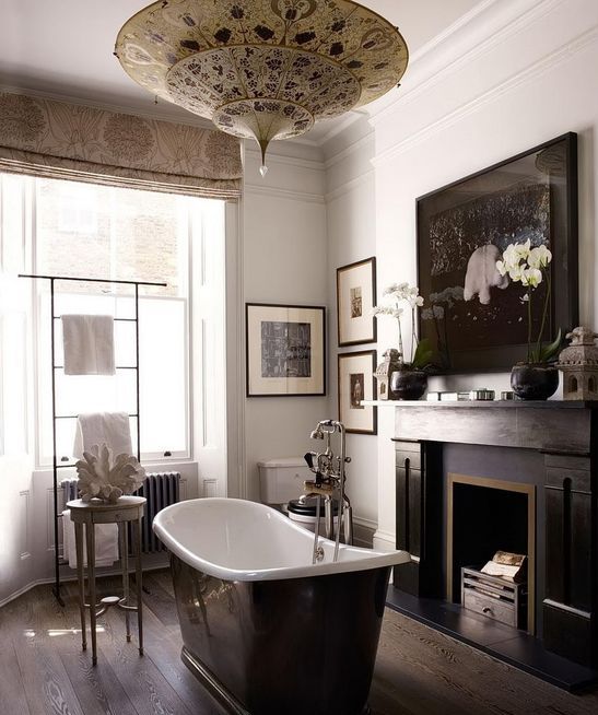 a moody vintage bathroom with a dark floor, a black fireplace, a black bathtub, a Moroccan pendant lamp and a gallery wall