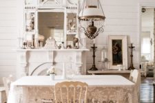 a neutral shabby chic dining room with white furniture, a vintage lamp, a large mirror and a faux fireplace and a lace tablecloth