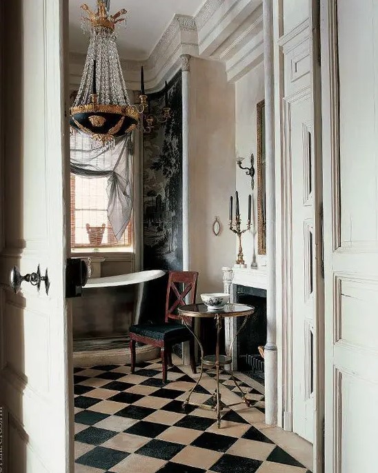 a neutral vintage bathroom with a faux fireplace, a shiny free-standing bathtub, a checked floor, a black chair, a crystal chandelier