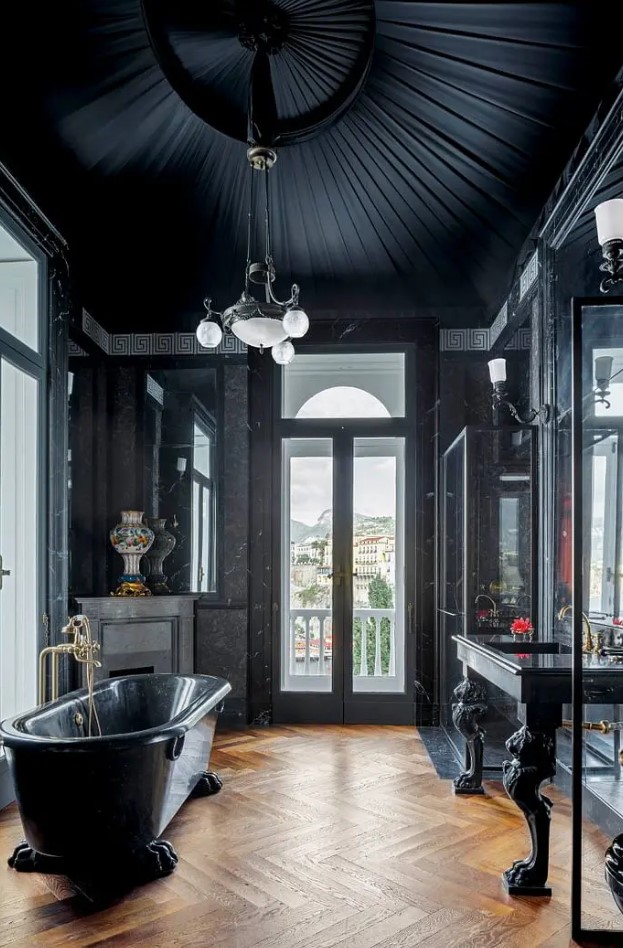 a quirky Gothic bathroom in black, with an attic textural ceiling, a black stone tub and black stone furniture with paws, with a fireplace and a large mirror