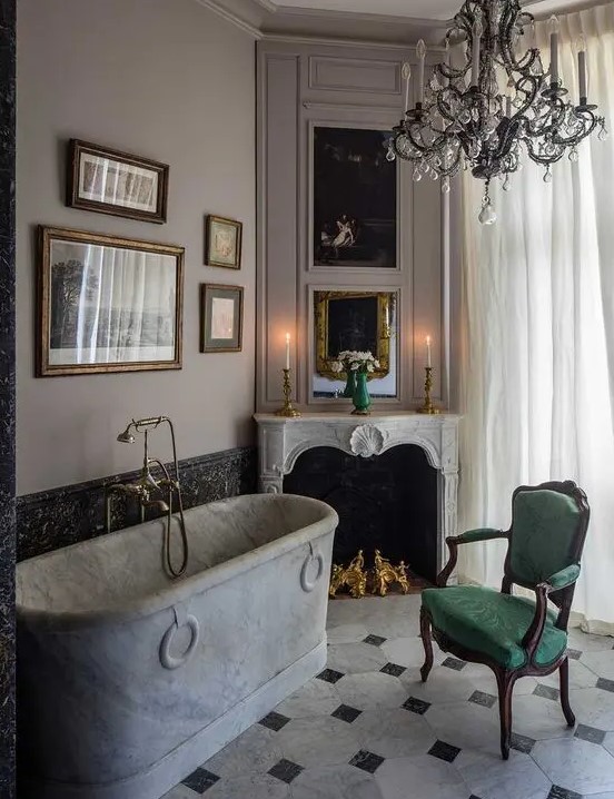 a refined vintage bathroom with a chic faux fireplace, a marble bathtub, a black chandelier, a gallery wall and a green chair