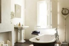 a refined vintage bathroom with a faux fireplace, a black clawfoot bathtub, a free-standing sink, a vintage chandelier and shutters on the window