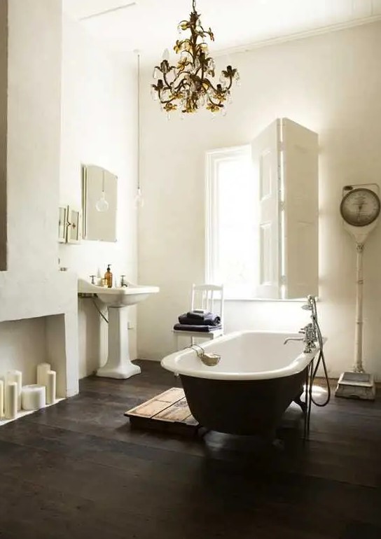 a refined vintage bathroom with a faux fireplace, a black clawfoot bathtub, a free standing sink, a vintage chandelier and shutters on the window