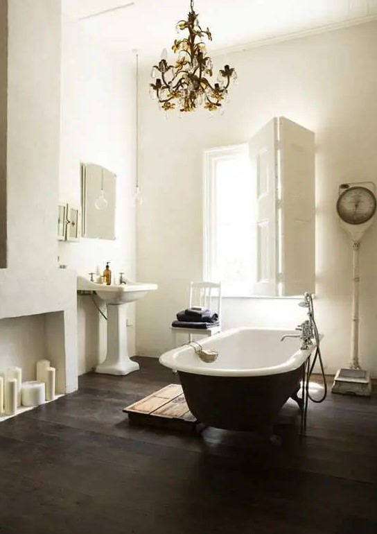 a refined vintage bathroom with a faux fireplace, a black clawfoot bathtub, a free-standing sink, a vintage chandelier and shutters on the window