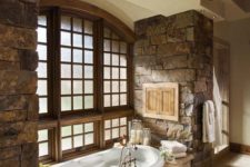 a rustic bathroom with rough stone walls, a built-in bathtub clad with tiles and a vintage lamp