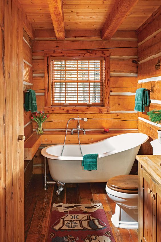 a small cabin bathroom clad with wood, with wooden beams, a wooden vanity, a clawfoot tub and bold textiles