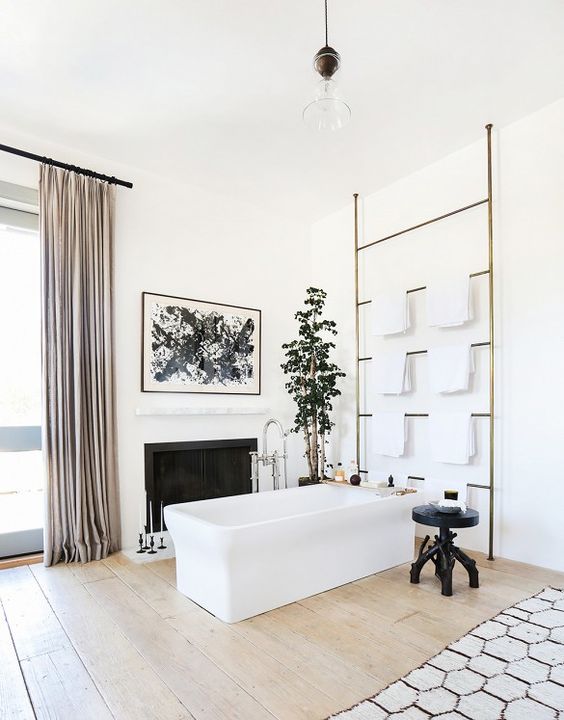 a sophisticated modern bathroom with a fireplace, a rectangular but, a large ladder for towels, a black carved table, a potted plant and blush curtains