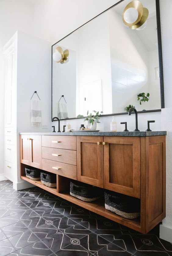 a stylish modern bathroom with a black tiled floor, a floating wooden vanity with a stone countertop, black fixtures and baskets for storage