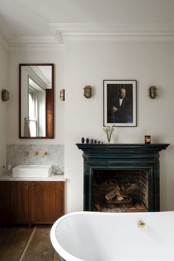 a vintage bathroom with a built in vanity and a mirror, a vintage fireplace with a teal mantel, an oval tub, a print and some decor