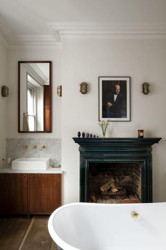 a vintage bathroom with a built-in vanity and a mirror, a vintage fireplace with a teal mantel, an oval tub, a print and some decor