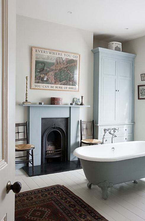 a vintage bathroom with a light blue wardrobe, a blue clawfoot bathtub, a fireplace with a blue mantel, artwork and a printed rug
