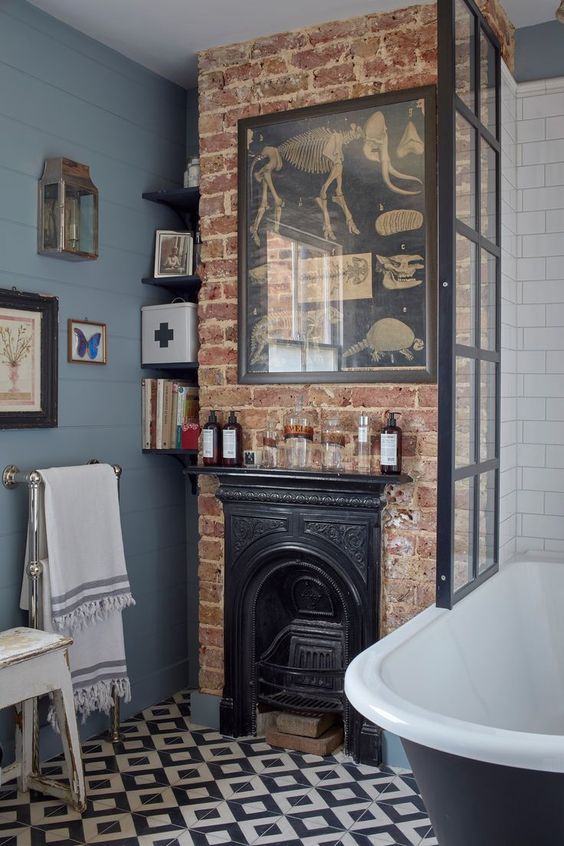 a vintage bathroom with blue walls, a brick wall with a fireplace, a black bathtub, vintage artwork and a black and white tile floor