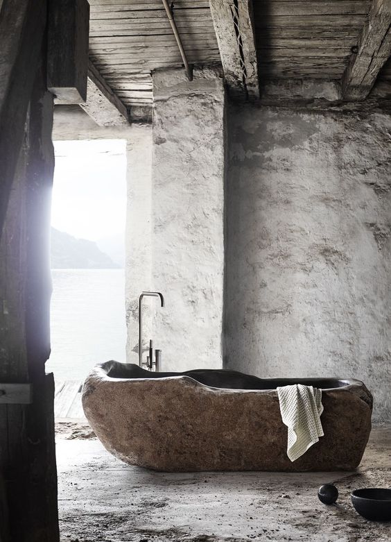 a wabi-sabi bathroom with plaster walls and a bathtub cut out of a stone slab is a unique idea to go for