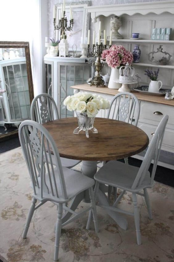 a welcoming shabby chic dining room with off-white furniture, candles in candelabras, a large mirror and blooms