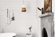 an eclectic bathroom with white planked walls, a fireplace with a concrete mantel, an oval tub, pendant lamps and a jute rug
