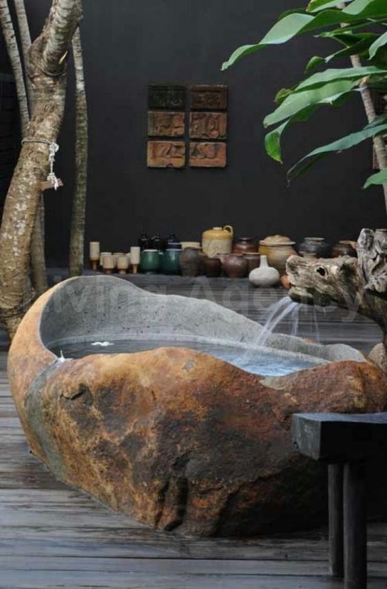 an outdoor tropical bathroom with a bathtub cut out of a stone slab, lots of pots and potted plants an outdoor tropical bathroom with a bathtub cut out of a stone slab, lots of pots and potted plants