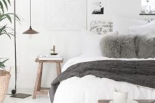 a Scandinavian bedroom with a white bed, some wooden furniture, pendant lamps, artworks and potted greenery