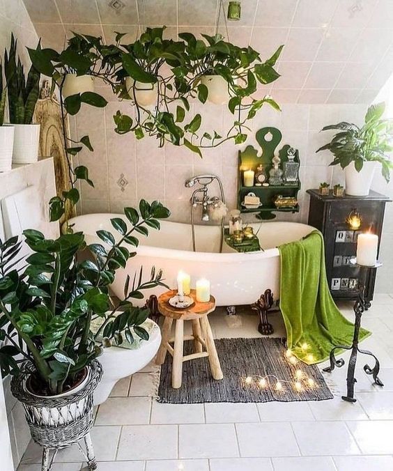 a boho chic bathroom with a vintage tub, some lights and candles, potted plants all around the tub and suspended