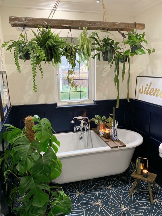 a bold navy and neutral bathroom with a tile floor, paneling and lots of potted green plants around the tub