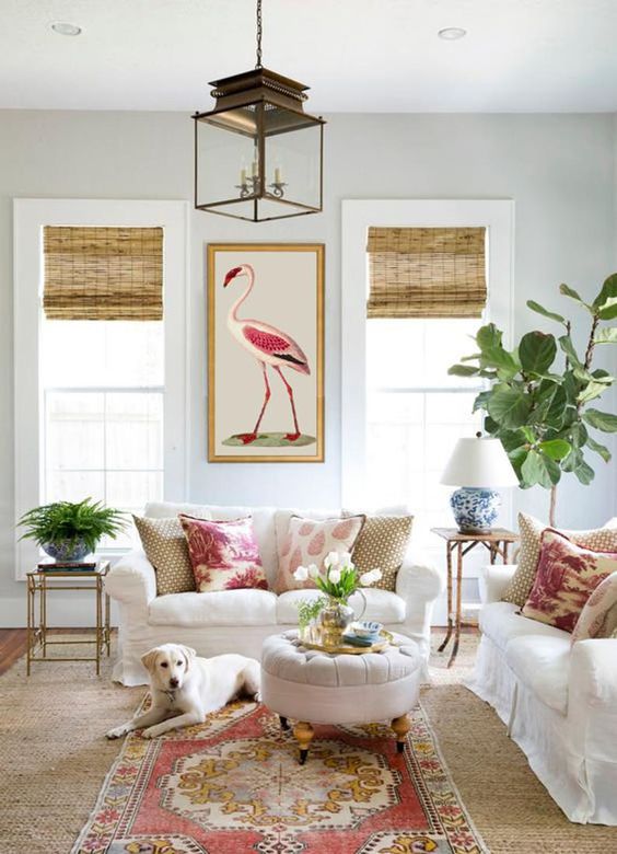 a bright and cool living room with white furniture, greenery and neutral blooms, a boho rug and printed curtains, a bold artwork