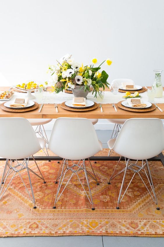 a bright and fresh spring table setting with a yellow and spring floral centerpiece, wicker chargers, a white runner and yellow napkins